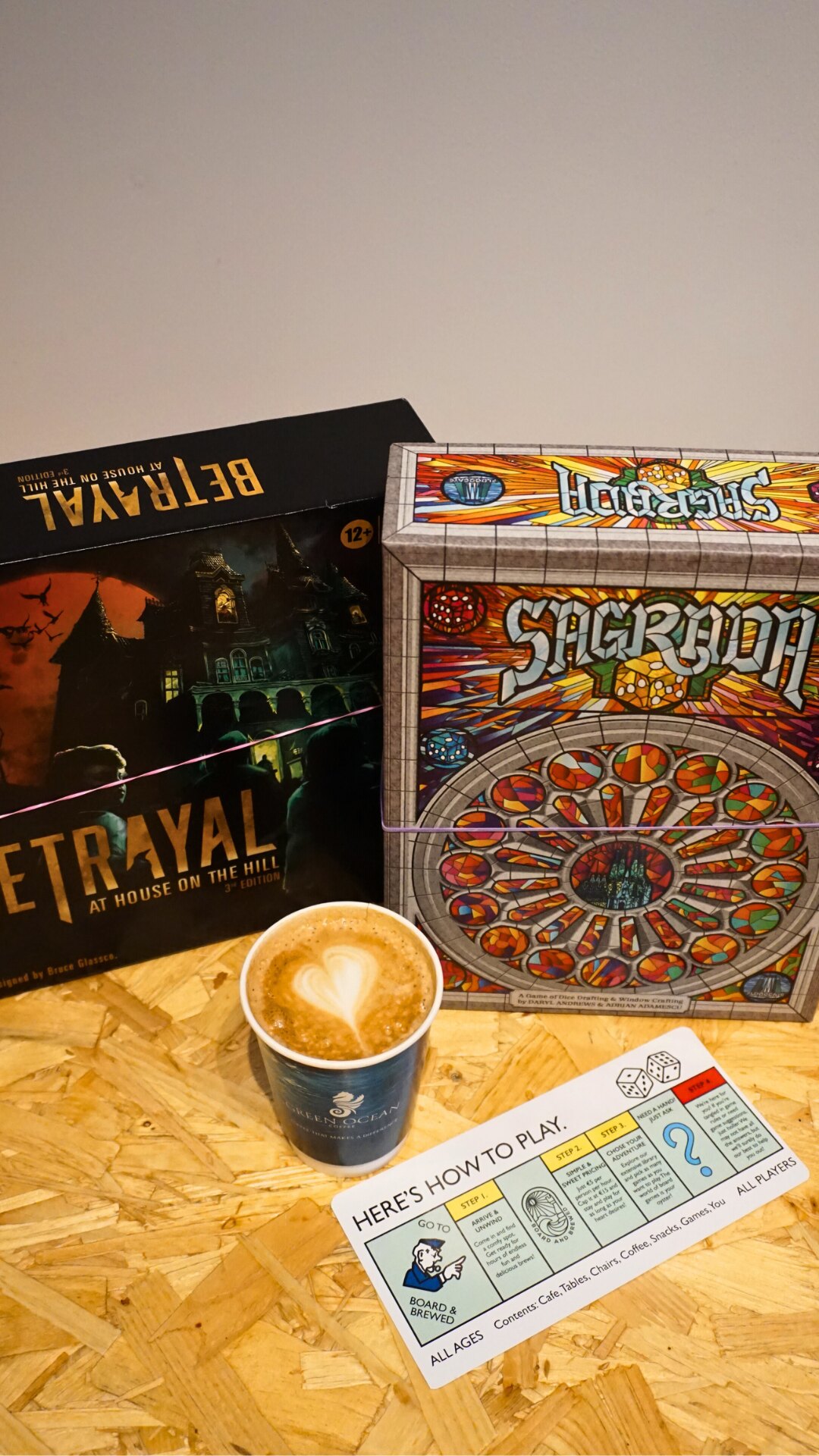 Betrayal and Sagrada board games beside a Board & Brewed latte